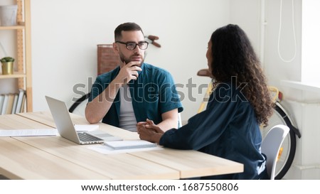 Thoughtful diverse colleagues sit at desk in office talk discuss business ideas at briefing together, pensive businesspeople brainstorm cooperate using laptop at meeting, collaboration concept Royalty-Free Stock Photo #1687550806