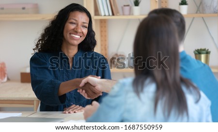 Smiling African American female real estate agent shake hand grating getting acquainted with clients at meeting, happy biracial woman consultant handshake close deal sign agreement with young couple Royalty-Free Stock Photo #1687550959