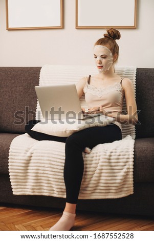 Caucasian woman wearing a special anti-wrinkle mask while sitting on the couch and using a computer