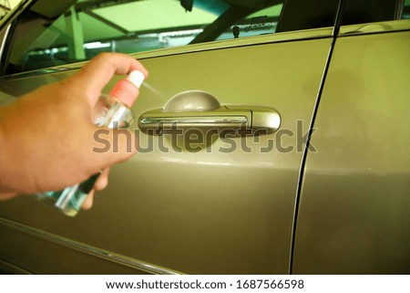 Car door handle With a man's hand spraying alcohol to kill the corona virus (Covid 19)