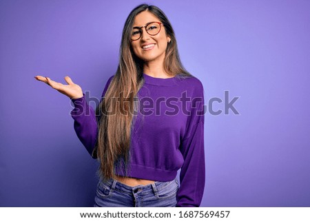 Young beautiful smart woman wearing glasses over purple isolated background smiling cheerful presenting and pointing with palm of hand looking at the camera.
