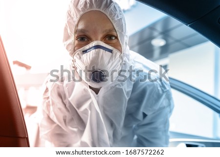 Portrait of tired exhausted female doctor, scientist or nurse wearing face mask and biological hazmat protective suit open car door on road outdoor. Coronavirus covid-19 outbreak alert danger Royalty-Free Stock Photo #1687572262