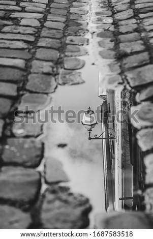 Black and white street mirror reflection in an old town. Reflection of the public lighting in a puddle of water - Tours, France 2020