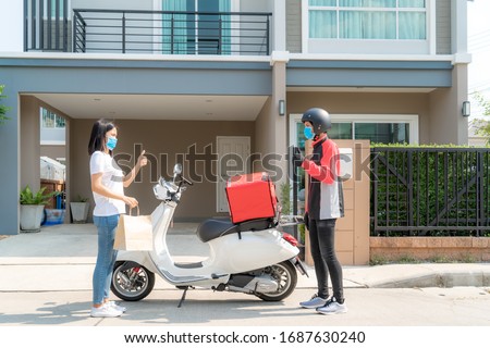 Asian woman pick up delivery food bag from box and thumb up form contactless or contact free from delivery rider with bicycle in front house for social distancing for infection risk. Royalty-Free Stock Photo #1687630240