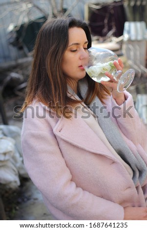 beautiful young woman in a pink coat with a glass in her hands in which there are white flowers and wine on a bright day