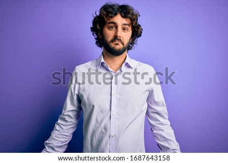 Young handsome business man with beard wearing shirt standing over purple background looking sleepy and tired, exhausted for fatigue and hangover, lazy eyes in the morning.