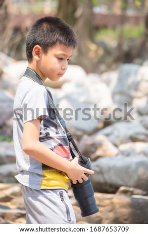 Asian boy holding a camera  Background blurry rocks and tree at Laem Kho Kwang Beach  in Chumphon , Thailand.