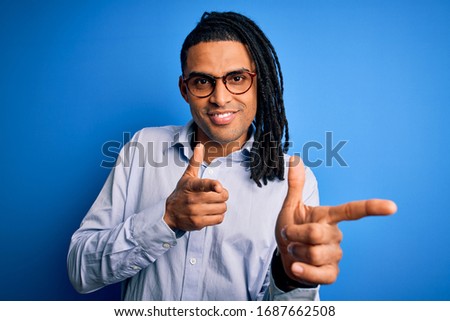 Young handsome african american man with dreadlocks wearing casual shirt and glasses pointing fingers to camera with happy and funny face. Good energy and vibes.