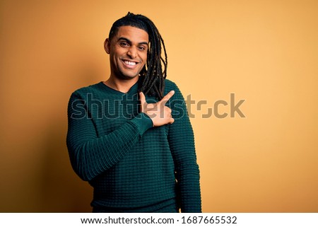 Young handsome african american afro man with dreadlocks wearing green casual sweater cheerful with a smile of face pointing with hand and finger up to the side with happy and natural expression