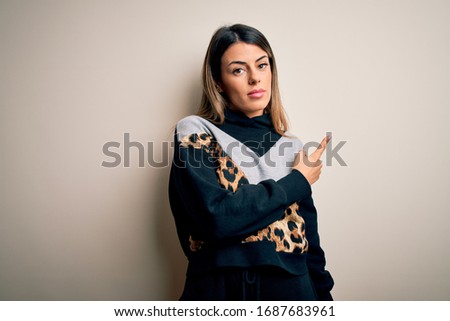 Young beautiful woman wearing casual sweatshirt standing over isolated white background Pointing with hand finger to the side showing advertisement, serious and calm face