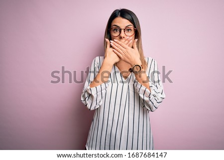 Young beautiful woman wearing casual striped t-shirt and glasses over pink background shocked covering mouth with hands for mistake. Secret concept.