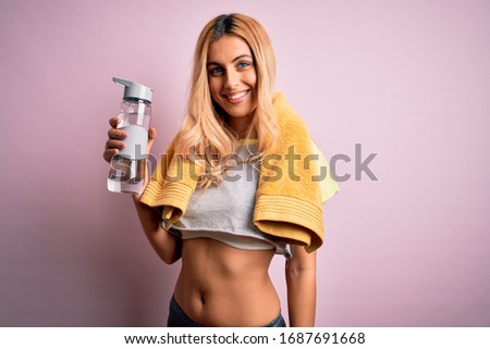 Young beautiful blonde sportswoman doing sport wearing sportswear drinking bottle of water with a happy face standing and smiling with a confident smile showing teeth