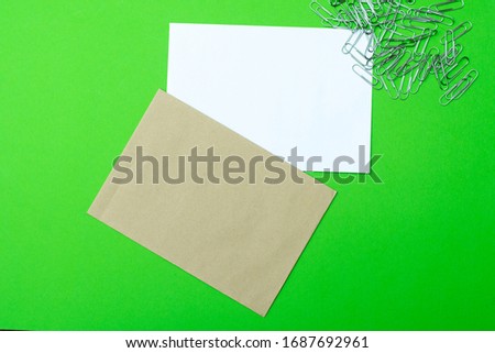 craft and white envelopes on a green background with a bunch of metal paper clips nearby. place for text