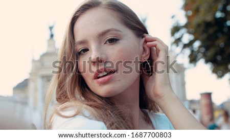 Lifestyle selfie portrait of young cute and pretty woman with curly golden hair posing and taking selfie on the street smiling and having fun