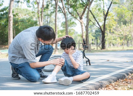 Young asian father of dad calms son that fell from the bike and he get injury on knee and leg while have weekend leisure in public park,accident can happen everywhere and every time. Royalty-Free Stock Photo #1687702459