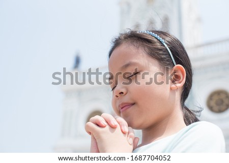 cute little girl praying. little girl praying in the morning. little asian girl hand praying. hands folded in prayer concept for faith. spirituality and religion in front of the church.