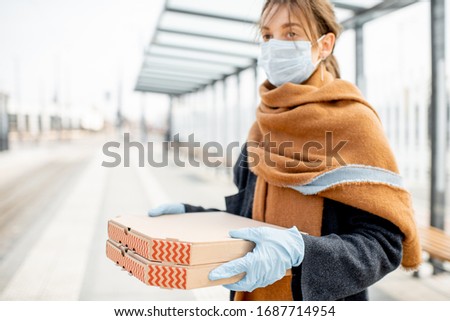 Young woman in medical mask and gloves holding cardboard with pizza's going out for food during the epidemic. Concept of takeaway food during quarantine