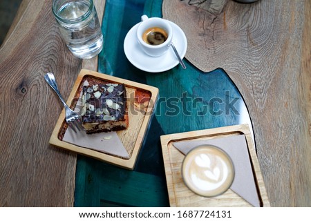 Two cups of coffee with latte art on design wooden background with fresh baked almond pastry bun and chocolate. Beautiful brunch in coffee shop on design epoxy blue river table. Royalty-Free Stock Photo #1687724131