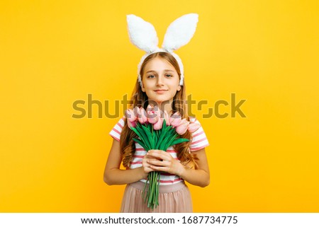 Happy beautiful girl on her head with rabbit ears, with a bouquet of tulips on a yellow background. Symbol of Easter and spring.