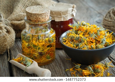 Bottles of calendula infusion or oil, healthy marigold flowers in bowl and calendula salve on wooden table. Herbal medicine.