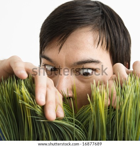 Asian young man looking through grass with determined expression.