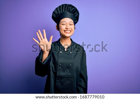 Young beautiful chinese chef woman wearing cooker uniform and hat over purple background showing and pointing up with fingers number five while smiling confident and happy.