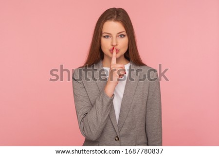 Shh, keep calm! Portrait of young woman in business suit keeping finger on lips making silence gesture, shushing asking to be quiet, secrecy concept. indoor studio shot isolated on pink background