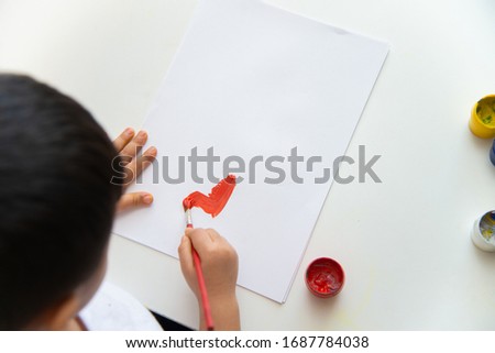 Little boy hand draws on paper. Cute Child boy is sitting and painting. Stay home.