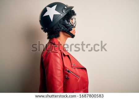 Young African American afro motorcyclist woman with curly hair wearing motorcycle helmet looking to side, relax profile pose with natural face with confident smile.