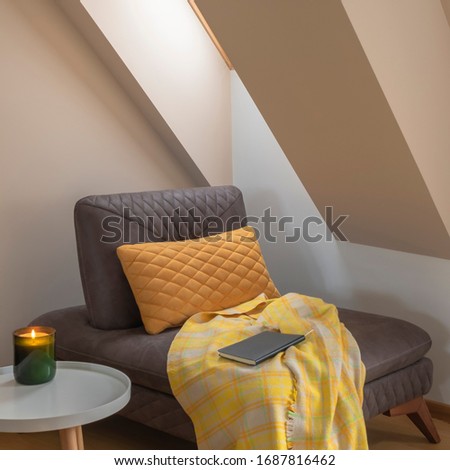 Cozy nook by the window with yellow blanket and pillow on a coach, candle on coffee table and book Royalty-Free Stock Photo #1687816462