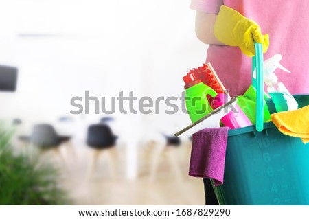 Charwoman standing with a bucket and cleaning products on blurred office background. Royalty-Free Stock Photo #1687829290