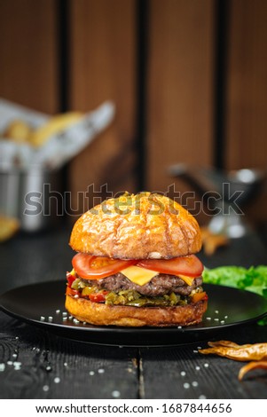 Appetizing juicy burger with jalapeno peppers on a black plate on a dark wooden table, upright, side view