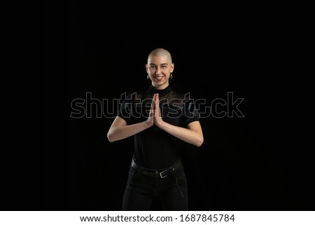 Praying, smiling. Monochrome portrait of young caucasian bald woman isolated on black studio background. Beautiful female model. Human emotions, facial expression, sales, ad concept. Youth culture.