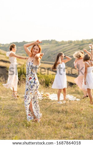The company of happy female friends having fun and dancing outside in a picnic at hills