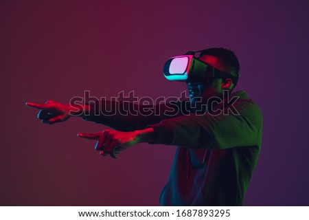 African-american man's portrait in VR-headset isolated on gradient studio background in neon light. Beautiful male model. Concept of human emotions, facial expression, sales, ad, inclusion, tech.