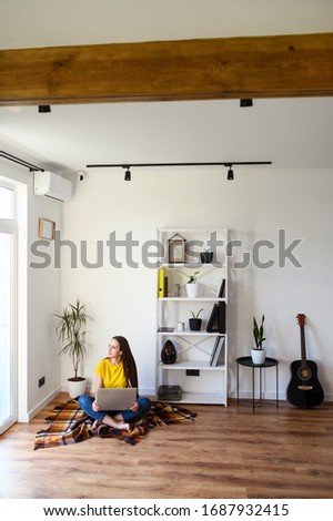 Freelancer woman works from home, work remotely. Young woman in casual clothes sitting with a laptop on a cozy plaid in a stylish minimalistic interior. Vertical photo