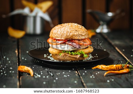 Delicious burger with fried egg, chicken cutlet and onion rings on the wooden table, horizontal, side view