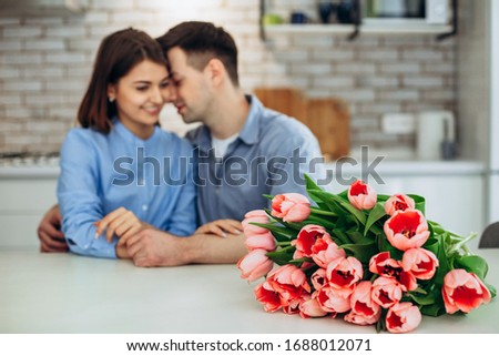 Surprise! Beautiful romantic couple at home. Young man is presenting flowers to his beloved. Feel of happiness