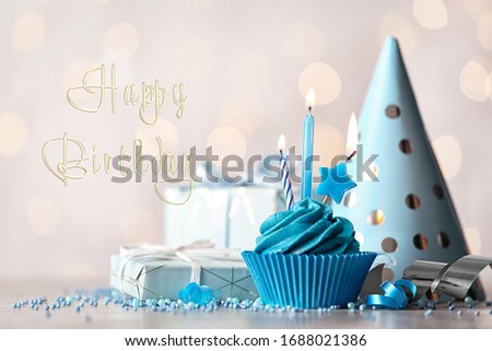 Delicious cupcake with burning candles and text Happy birthday on blurred background