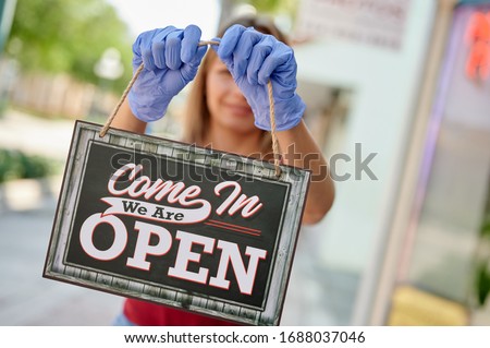 Woman in blue gloves holding a nameplate "we are open", focus on nameplate