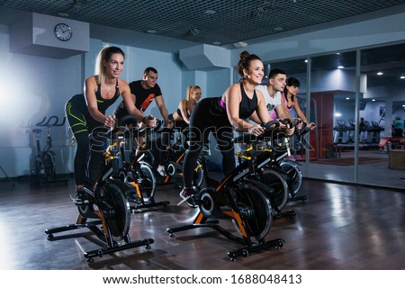 Cycling class in fitness club, group of fit people spinning on cardio machine. Man and women do sports exercises at gym fat burning class. Active lifestyle, health care and body training concept Royalty-Free Stock Photo #1688048413