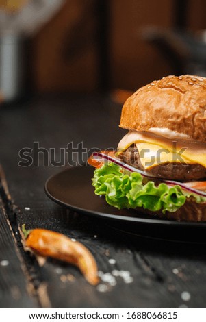 Half classic delicious burger on a black plate on the wooden table, upright, side view