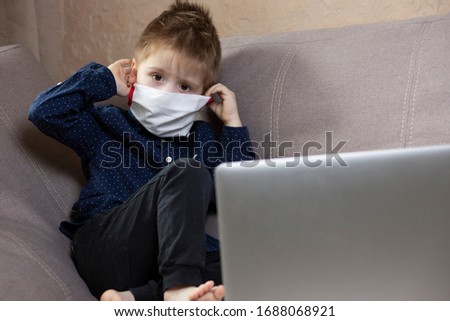 little boy in a white medical mask sits near a laptop