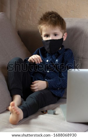 a boy in a medical mask sits near a laptop