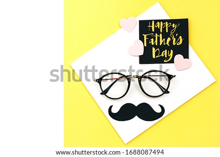 Close up of eyeglasses, stylish black paper photo booth props moustaches, many little hearts and card with phrase happy father's day on yellow background. Copy space for inscriptions. Creative idea.