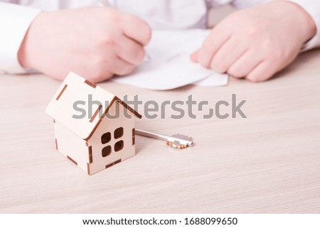 a man in a shirt signs a mortgage or insurance contract or a contract of sale when buying a new house or selling a house, background in blur, small wooden model of the house and the key