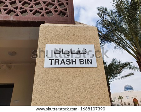 Trash bin stand sign board on the wall in English and Arabic language 
