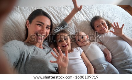 Authentic close up of happy mother with her kids are making a selfie or video call to father or relatives in a bed. Concept of technology, new generation,family, connection, parenthood, authenticity