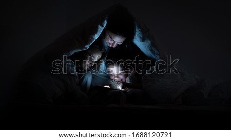 Portrait of happy mother and her daughters using a tablet in the dark  under the blanket. Concept of family, entertainment, education, technology, motherhood