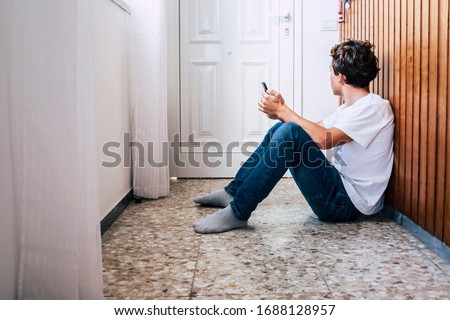 People inside home for stayhome lockdown emergency coronavirus - young man sit down on the. floor with a phone looking at the door hope and wait to go out and enjoy life Royalty-Free Stock Photo #1688128957